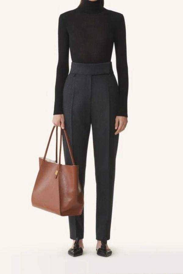 Front view of black turtleneck jumper on model wearing grey pants and flats, against a white background.