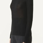 Side view of black turtleneck jumper on model wearing grey pants, against a white background.