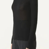 Side view of black turtleneck jumper on model wearing grey pants, against a white background.