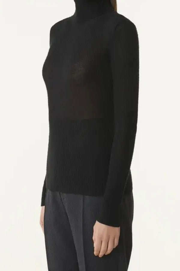 Side view of black turtleneck jumper on model wearing grey pants, against a white background.