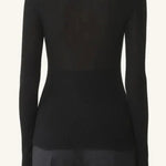 Back view of black turtleneck jumper on model wearing grey pants, against a white background.