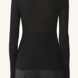 Back view of black turtleneck jumper on model wearing grey pants, against a white background.