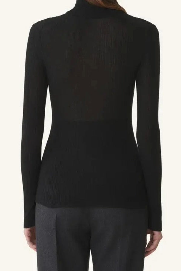 Back view of black turtleneck jumper on model wearing grey pants, against a white background.