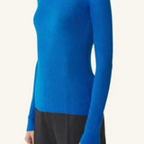 Side view of electric blue turtleneck jumper on model wearing grey pants, against a white background.