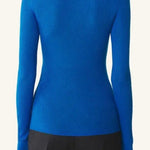 Back view of electric blue turtleneck jumper on model wearing grey pants, against a white background.