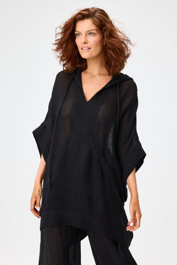 Front view of black hooded poncho on model wearing black pants, against a white background.