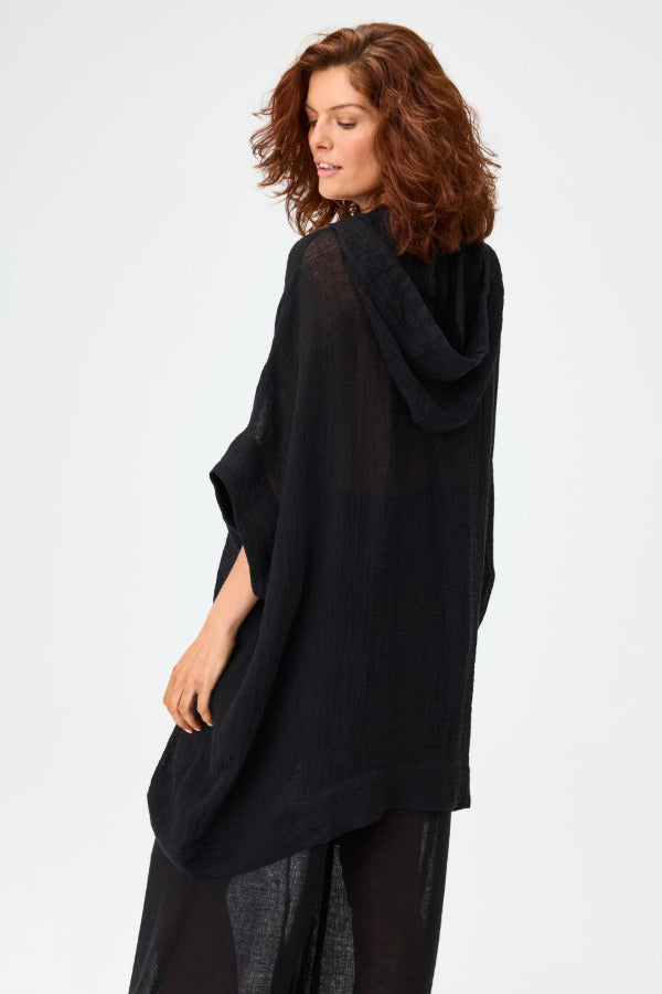 Back view of black hooded poncho on model wearing black pants, against a white background.