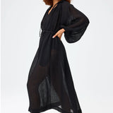 Side view of black maxi poet dress on brown-haired model wearing brown sandals, against a white background.