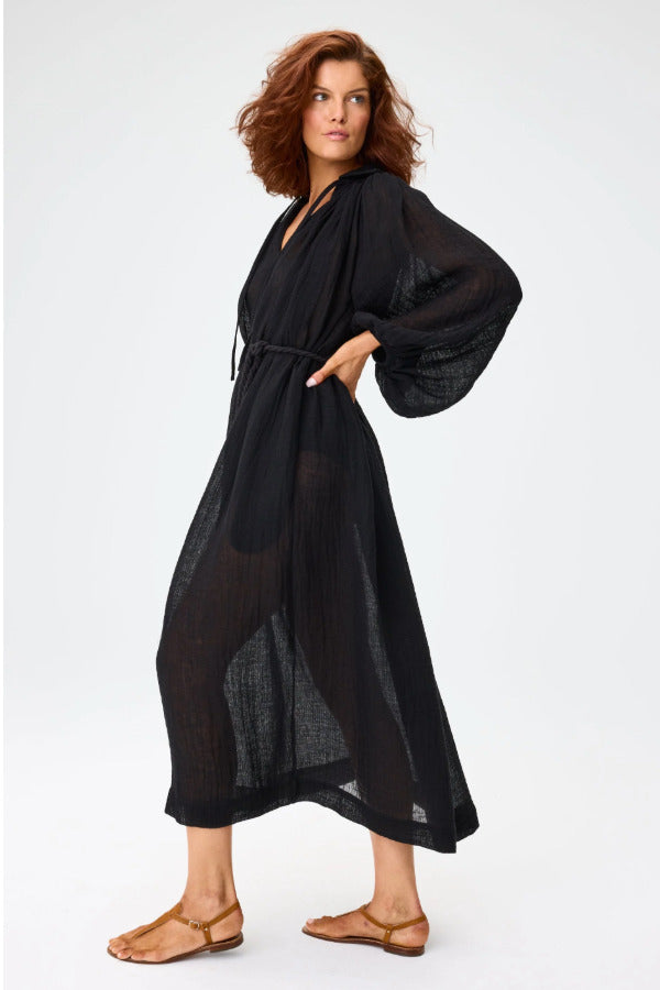 Side view of black maxi poet dress on brown-haired model wearing brown sandals, against a white background.