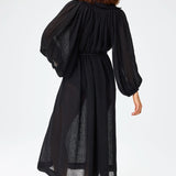 Back view of black maxi poet dress on brown-haired model wearing brown sandals against a white background.