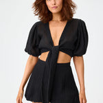 Front view of black pouf tie blouse on brown haired model wearing black shorts, against a white background.