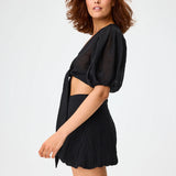 Side view of black pouf tie blouse on brown-haired model wearing black shorts, against a white background.