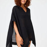 Front view of black short beach poncho on brown-haired model wearing black swim suit, against a white background.