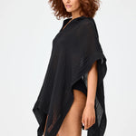 Side view of black short beach poncho on brown-haired model wearing black swim suit, against white background.