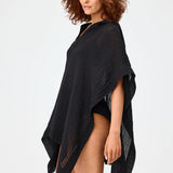 Side view of black short beach poncho on brown-haired model wearing black swim suit, against white background.