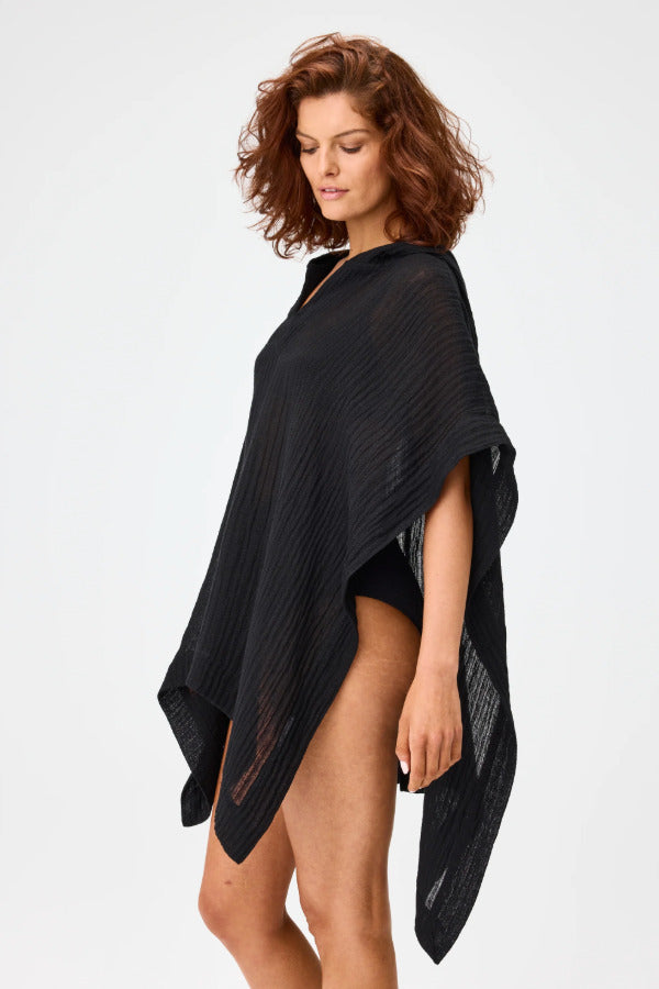 Side view of black short beach poncho on brown-haired model wearing black swim suit, against white background.