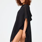 Side view of black short beach poncho on brown-haired model wearing black swim suit, against a white background.