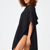Side view of black short beach poncho on brown-haired model wearing black swim suit, against a white background.
