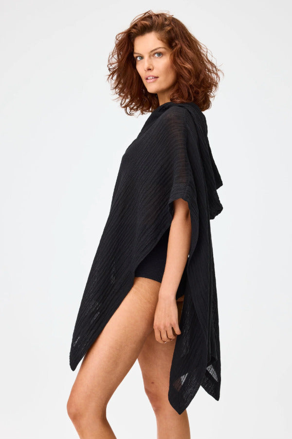 Side view of black short beach poncho on brown-haired model wearing black swim suit, against a white background.