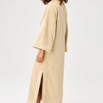 Back view of sand terry tunic caftan on model wearing brown sandals, against a white background.