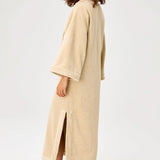 Back view of sand terry tunic caftan on model wearing brown sandals, against a white background.