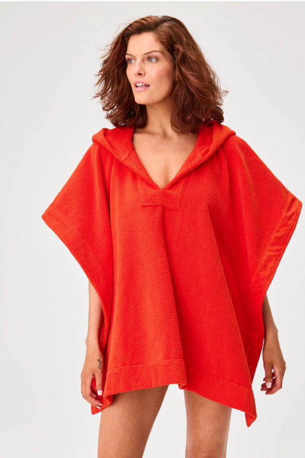 Front view of tomato terry short beach poncho on brown-haired model wearing navy swim suit, against a white background.