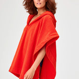 Side view of tomato terry short beach poncho on brown-haired model wearing navy swim suit, against a white background.