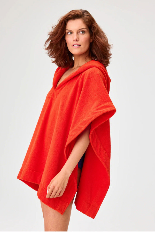 Side view of tomato terry short beach poncho on brown-haired model wearing navy swim suit, against a white background.