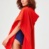 Back view of tomato terry short beach poncho on brown-haired model wearing navy swim suit, against a white background.
