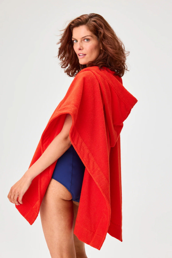 Back view of tomato terry short beach poncho on brown-haired model wearing navy swim suit, against a white background.