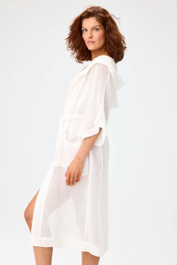Side view of white hooded dressing gown on brown-haired model wearing a white swim suit, against a white background.