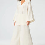 Front view of white low waist wide leg pant on brown-haired model wearing white top and brown sandals, against a white background.