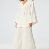 Front view of white low waist wide leg pant on brown-haired model wearing white top and brown sandals, against a white background.