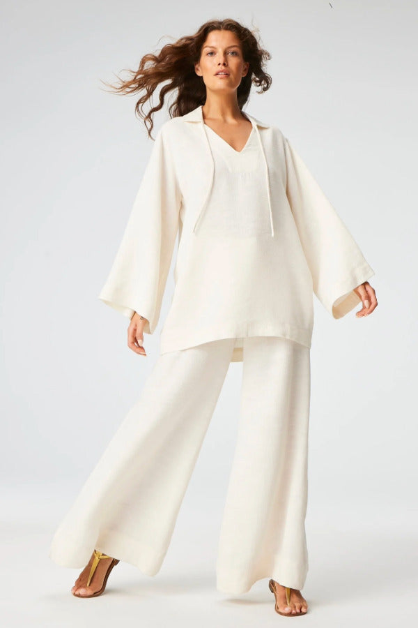 Front view of white low-wiast wide leg pant on brown-haired model wearing a white top and brown sandals, against a white background.