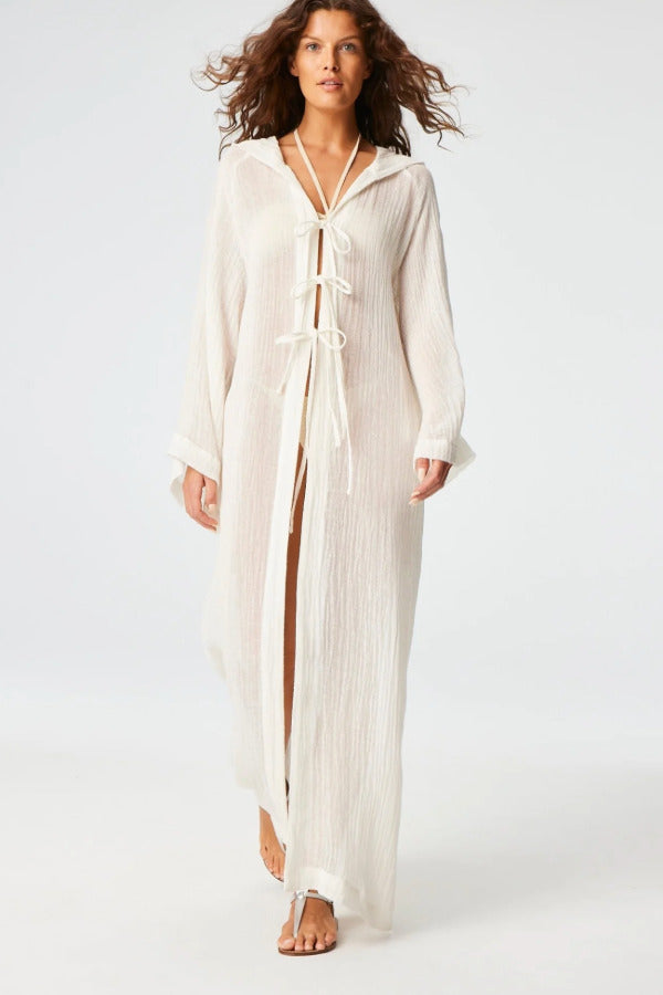 Front view of white maxi beach cape on brown-haired model wearing white swim suit and silver sandals, against a white background.