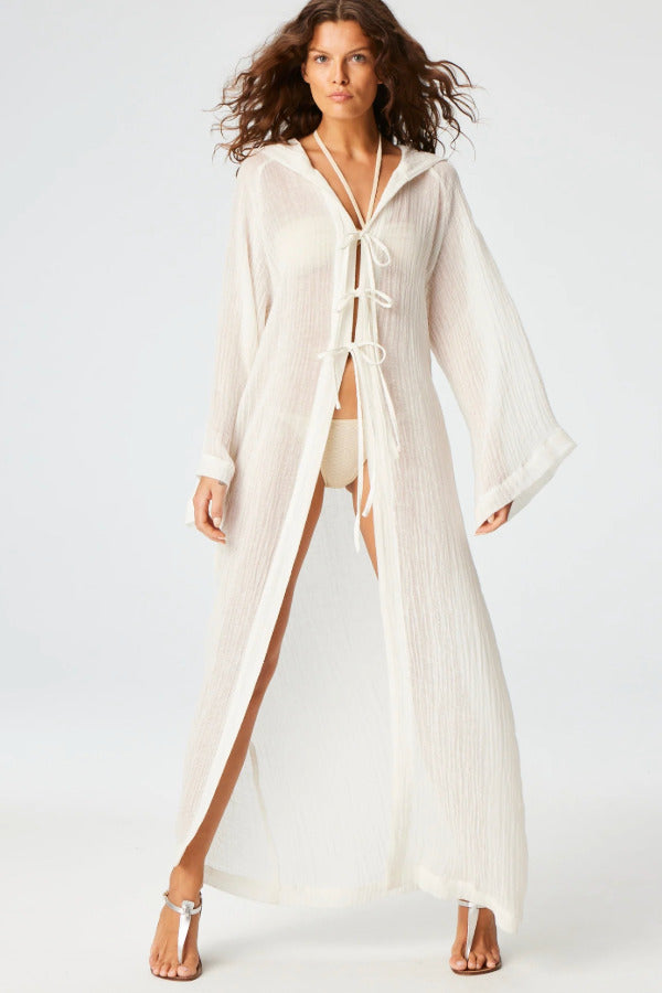 Front view of white maxi beach cape on brown-haired model wearing white swim suit and silver sandals, against a white background.