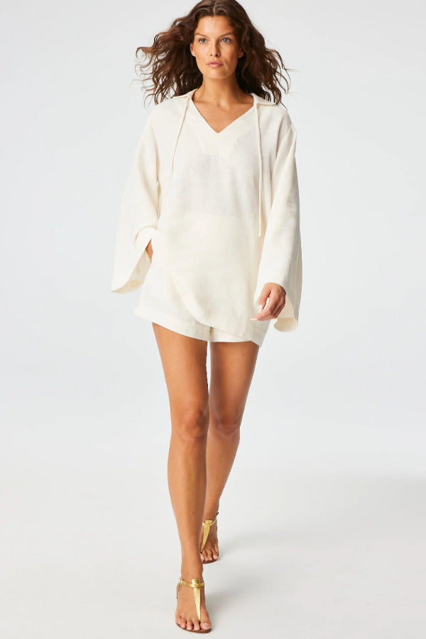 Front view of white mini short on brown-haired model wearing white tunic and gold sandals, against a white background.