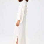 Side view of white tunic caftan on brown-haired model wearing silver sandals, against a white background.