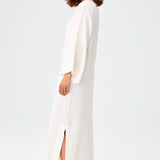 Side view of white tunic caftan on brown-haired model wearing silver sandals, against a white background.