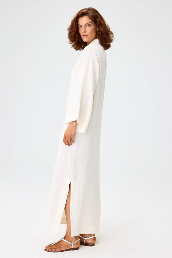 Side view of white tunic caftan on brown-haired model wearing silver sandals, against a white background.