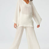 Front view of white tunic top on brown-haired model wearing white pants and silver sandals, against a white background.