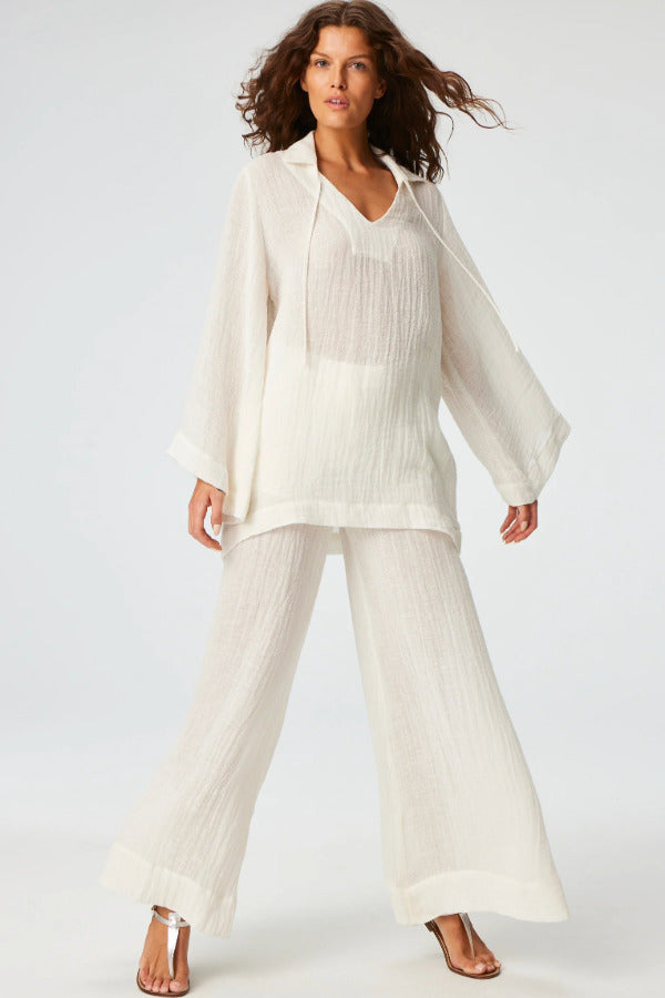 Front view of white tunic top on brown-haired model wearing white pants and silver sandals, against a white background.