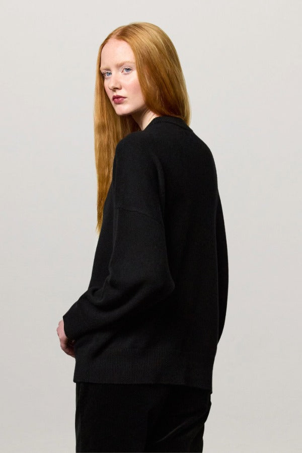 Back view of nero amelia rn sweater on model wearing black pants, against a white background.