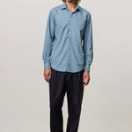 Front view of blue rain canary shirt on model wearing black trousers and brown suede shoes, against a white background.
