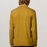 Back view of saffron ischia ls polo shirt on model wearing brown tweed trousers, against a white background.
