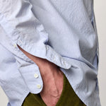 Side closeup view of azzurro canary classic shirt on model wearing green pants, against a white background.