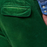 Back closeup view of green ionio2 trouser on model wearing blue shirt, against a white background.
