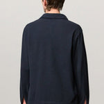 Back view of dark blue ischia ls polo shirt on model wearing milk pants, against a white background.