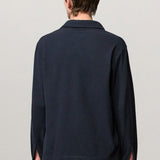 Back view of dark blue ischia ls polo shirt on model wearing milk pants, against a white background.