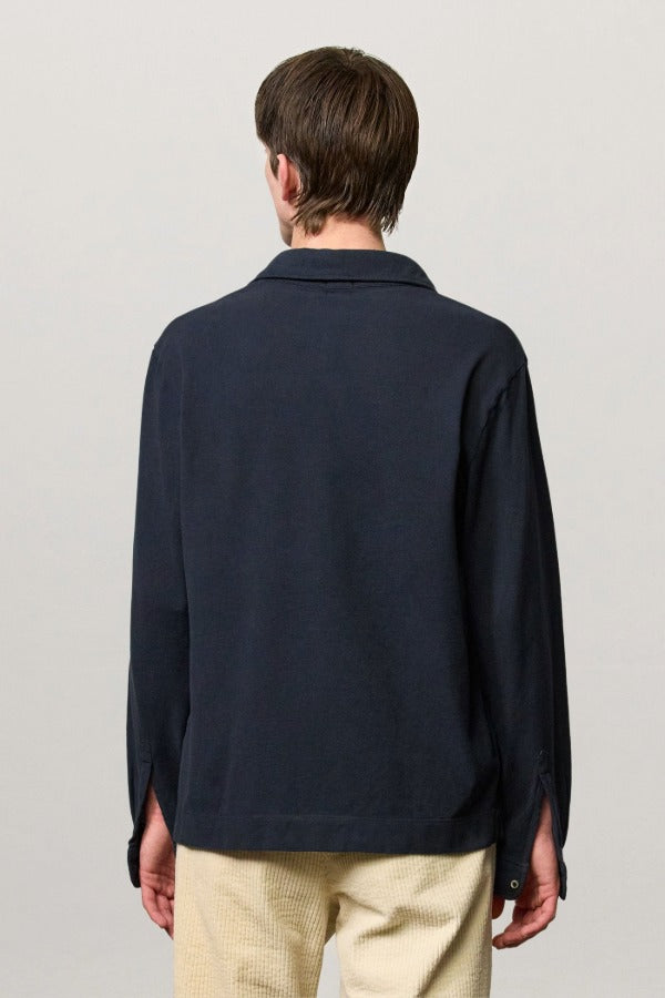 Back view of dark blue ischia ls polo shirt on model wearing milk pants, against a white background.
